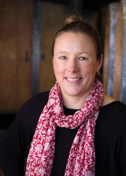 Weinproduzentin mit Schal im Weinkeller, lächelnd